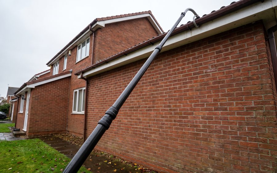A rigid vacuum pole reaching from the ground to the gutter of a two storey house