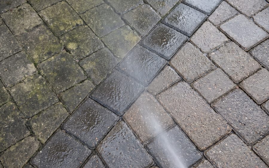 Grey block paving half cleaned, the cleaned strip lighter than the weathered surface